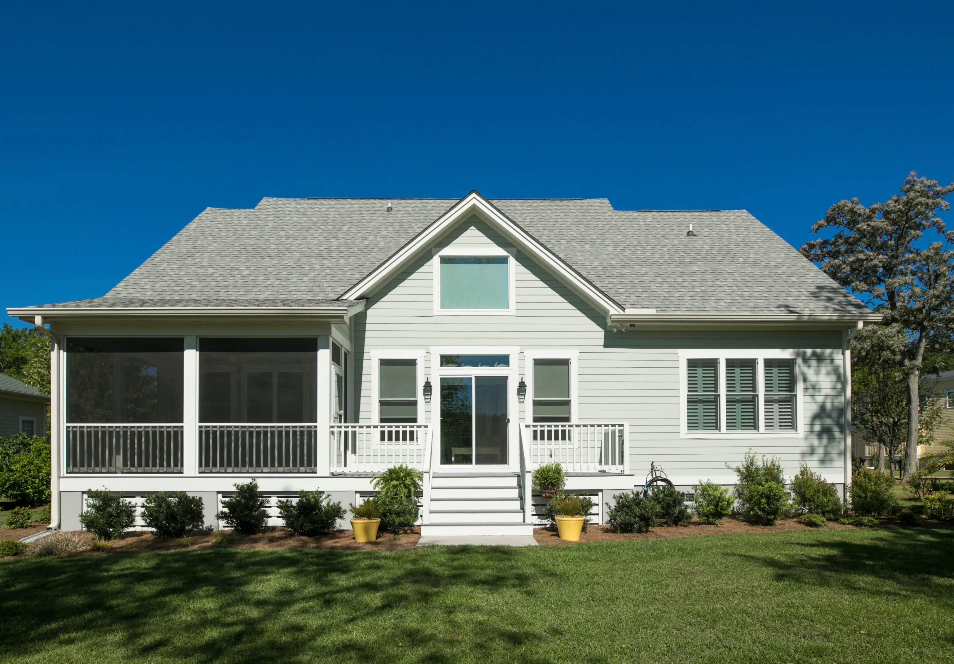 A charming white house with a porch and a well-maintained lawn under a clear blue sky.