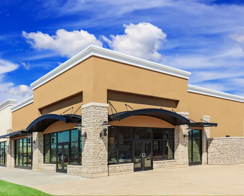 Modern commercial building with stone pillars and large windows under a blue sky.